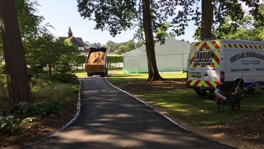 A dumper truck applying tarmac with workmen in the background